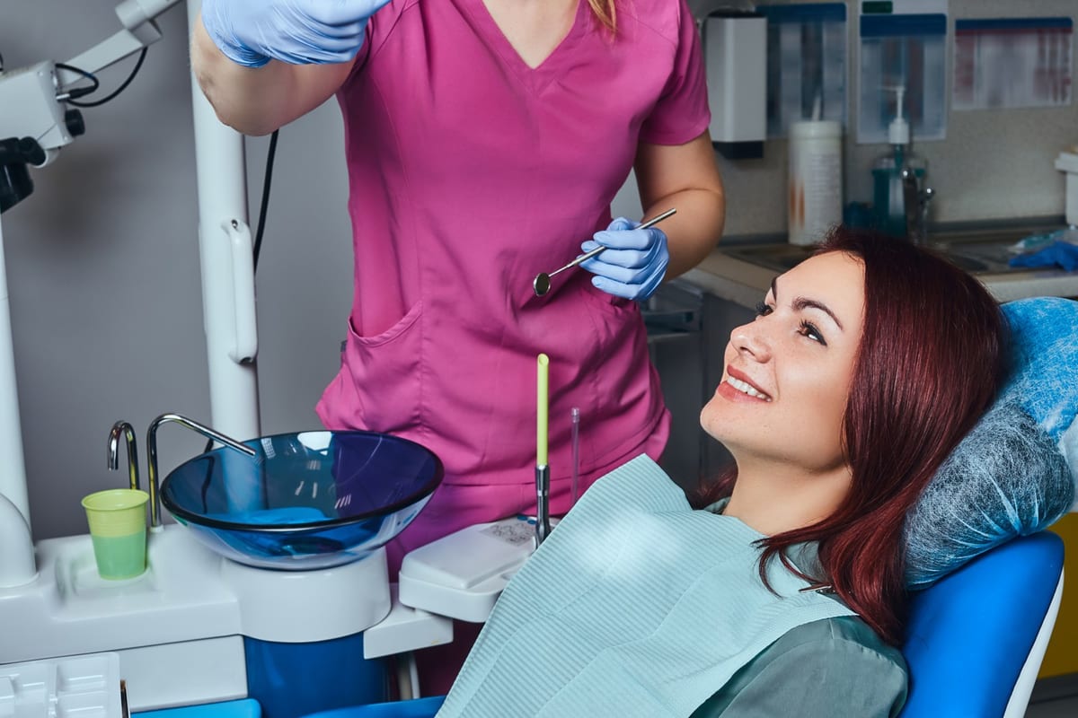 A hygienist working on a reclined patient's teeth with a scaler and mirror
